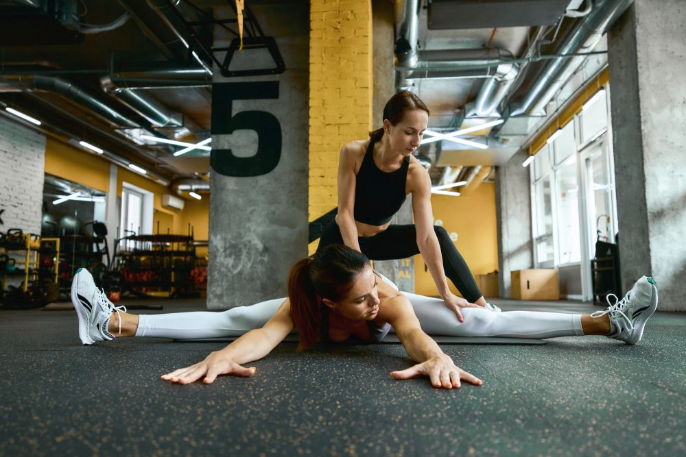 Young beautiful fitness woman in sportswear sitting on yoga mat at gym and doing stretching