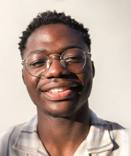 Headshot of young happy and smiling black man wearing glasses outdoors.